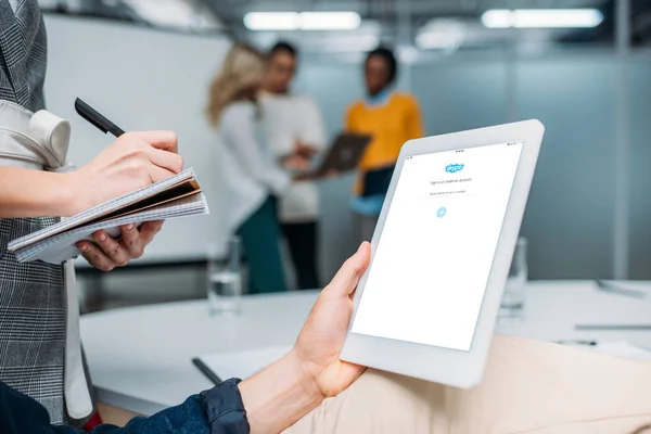 Hombre de negocios celebración de la tableta con Skype en la pantalla en la oficina moderna, mientras que el colega toma notas - foto de stock