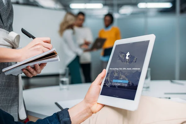Бизнесмен держит планшет с tumblr на экране в современном офисе, в то время как коллега делает заметки — стоковое фото