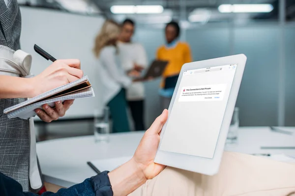 Businessman holding tablet with browser app on screen at modern office while colleague making notes — Stock Photo