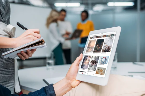 Empresário segurando tablet com pinterest na tela no escritório moderno, enquanto colega fazendo anotações — Fotografia de Stock