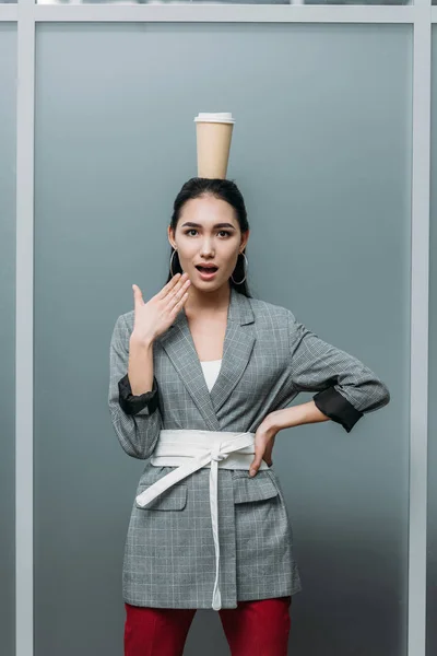 Sorprendida mujer asiática con taza de café desechable en la cabeza - foto de stock