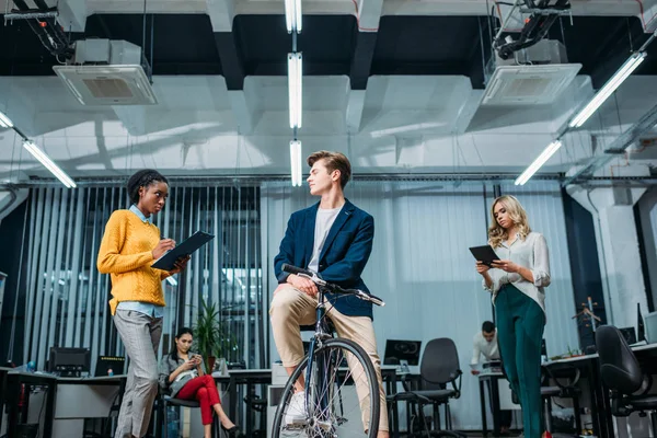 Young businessman with bike at modern office with partners standing around — Stock Photo
