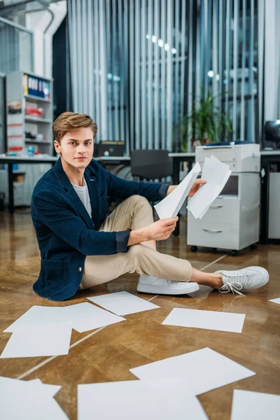 Bonito jovem empresário sentado no chão e fazendo papelada — Fotografia de Stock