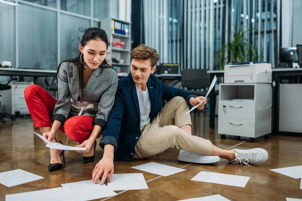 Jóvenes socios de negocios haciendo papeleo mientras están sentados en el piso de la oficina - foto de stock