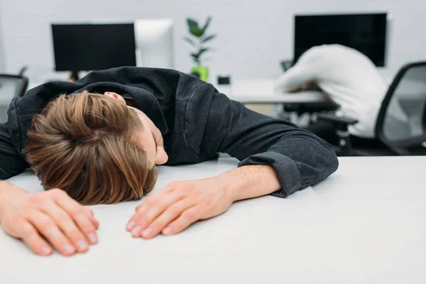 Exceso de trabajo joven gerente durmiendo en el trabajo en la oficina moderna - foto de stock