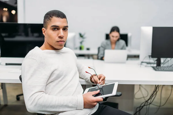 Schöner junger Geschäftsmann mit Tablet sitzt im Großraumbüro — Stockfoto