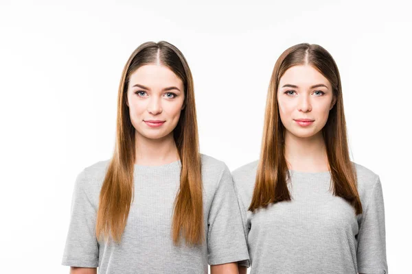 Портрет молодых улыбающихся близнецов в серых футболках, смотрящих в камеру, изолированную на белом — стоковое фото
