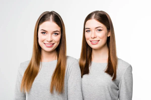 Retrato de gemelos sonrientes jóvenes en camisetas grises mirando a la cámara - foto de stock
