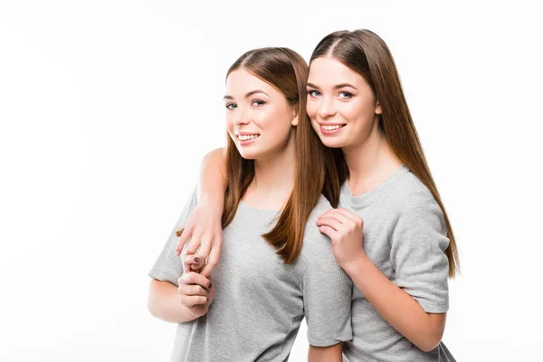 Портрет молодих усміхнених близнюків, що спираються один на одного і дивляться на камеру ізольовано на білому — стокове фото