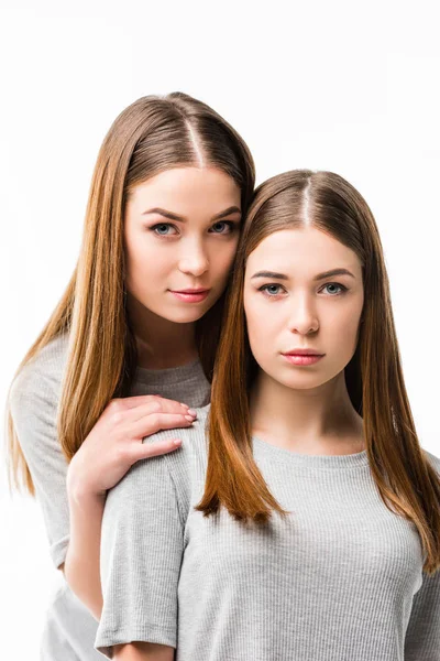 Portrait of young pensive woman hugging twin sister isolated on white — Stock Photo