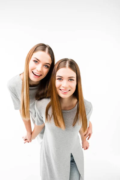 Porträt glücklicher Zwillinge in grauen T-Shirts, die sich an den Händen halten und isoliert auf weiß in die Kamera schauen — Stockfoto