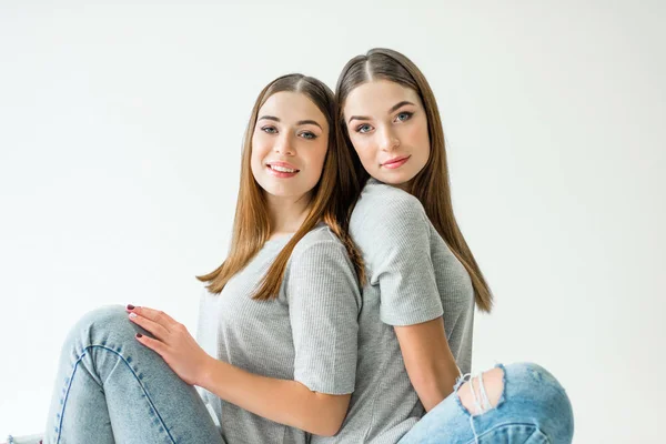 Portrait of attractive twin sisters in grey tshirts sitting back to back — Stock Photo