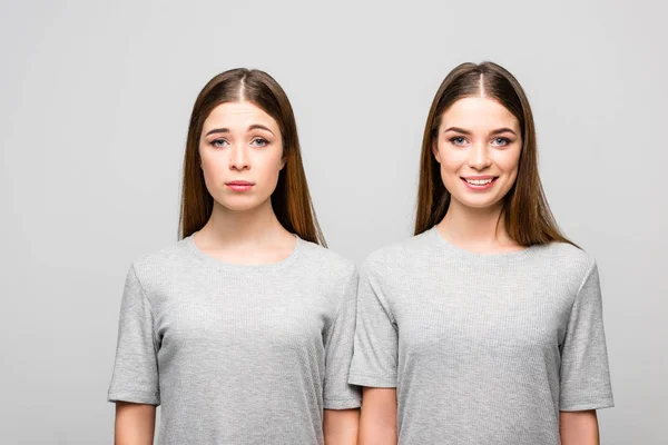 Portrait of twin sisters in grey tshirts showing emotions isolated on grey — Stock Photo