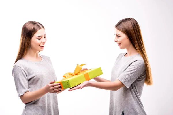 Vue latérale d'une femme souriante présentant un cadeau emballé à sa sœur jumelle — Photo de stock