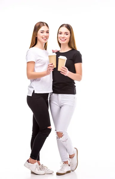 Fröhliche Zwillinge mit Kaffee to go in den Händen, die isoliert auf weiß in die Kamera schauen — Stockfoto