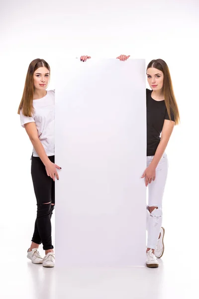 Молодые близнецы смотрят в камеру, держась за пустой баннер — стоковое фото