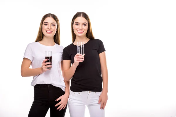 Retrato de gemelos alegres sosteniendo vasos de soda y agua en manos aisladas en blanco - foto de stock