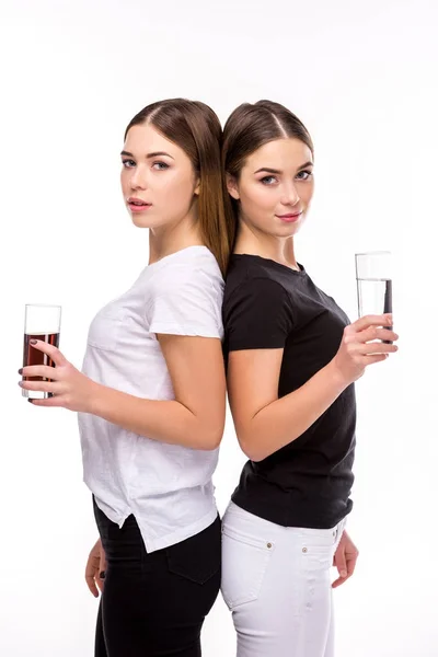 Portrait of beautiful twins holding glasses of soda and water in hands isolated on white — Stock Photo