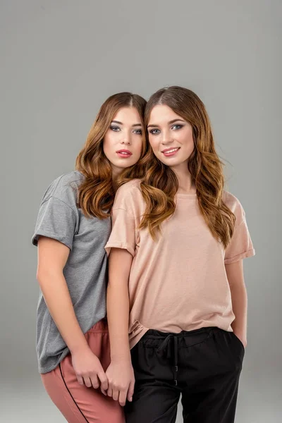 Portrait of beautiful twin sisters in stylish clothing isolated on grey — Stock Photo