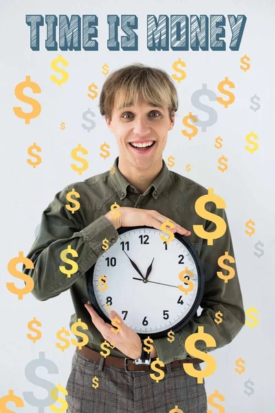 Усміхнений бізнесмен тримає настінний годинник в руках на білому з доларовими знаками, що летять навколо — стокове фото