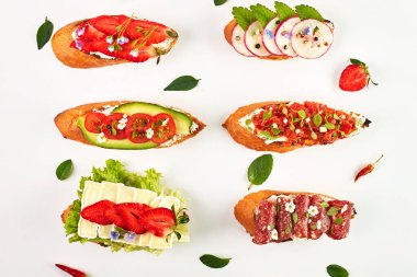 Domatesli, çilekli, avokadolu, turplu, peynirli ve jambonlu bruschetta. Beyaz bir arkaplanda, üst görünümde, yakın plan.