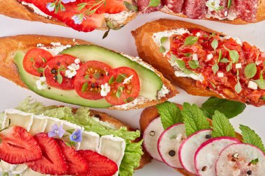 Domatesli, çilekli, avokadolu, turplu, peynirli ve jambonlu bruschetta. Beyaz bir arkaplanda, üst görünümde, yakın plan.