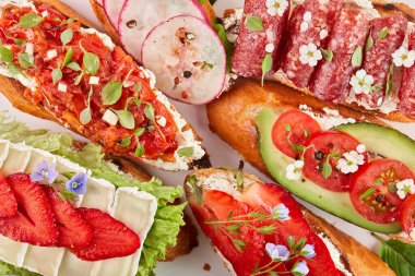 Domatesli, çilekli, avokadolu, turplu, peynirli ve jambonlu bruschetta. Beyaz bir arkaplanda, üst görünümde, yakın plan.