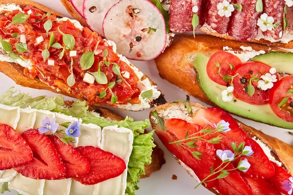 Assorted delicious bruschetta with tomatoes, strawberries, avocado, radish, Camembert and prosciutto. Close-up, top view, on a white background