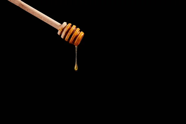 木製の蜂蜜のディッパー 黒の背景に蜂蜜を流れる — ストック写真