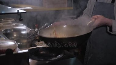Şef savurma Fried sebze ve et ile bir tavada, yangın ticari mutfak pişirme
