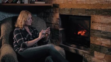 Şöminenin yanında evde, tatil ve yaşam tarzı kavramı oturan Smartphone kullanan güzel kadın