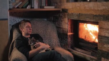Şöminenin yanında oturan ve şirin kedi bir ülkede evde sarılma genç adam