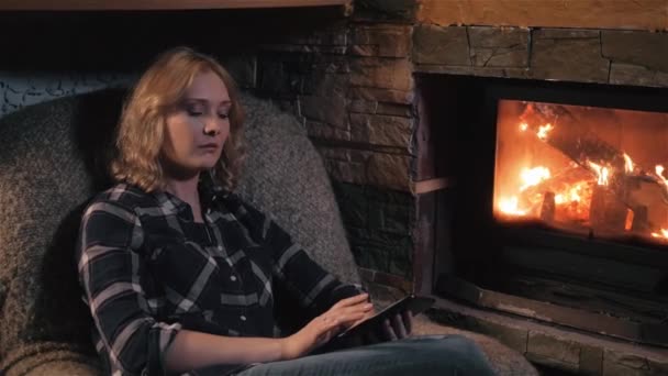 Mujer joven usando tableta digital sentada junto a la chimenea en casa — Vídeo de stock