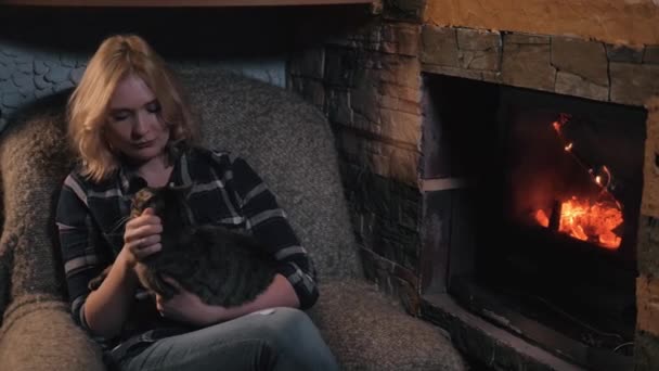 Молода красива жінка сидить біля каміна і переслідує милого кота в заміському будинку — стокове відео