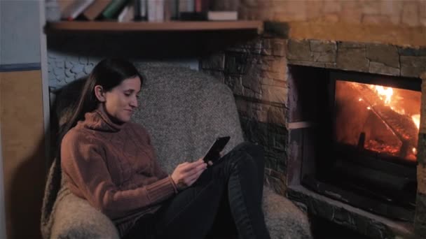 Ung kvinna med Digital tablett sitta vid öppna spisen hemma — Stockvideo