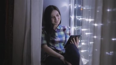 Güzel çekici kadın kullanarak Tablet Pc ve çelenk, Skype iletişim ile dekore pencere üzerinde oturan