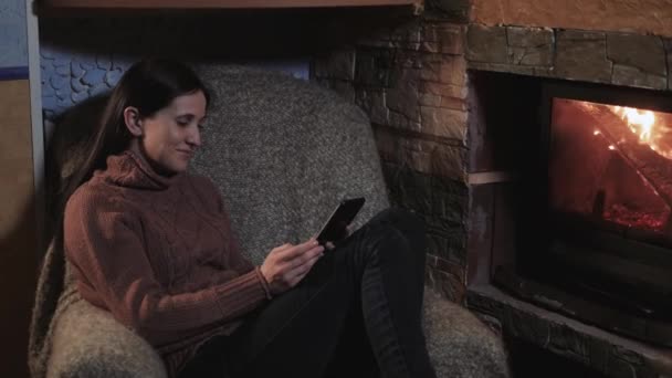 使用数字平板电脑，坐在家中壁炉旁的年轻女人 — 图库视频影像