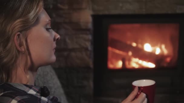 Jeune belle femme appréciant la boisson chaude d'hiver se détendre par cheminée à la maison, gros plan — Video