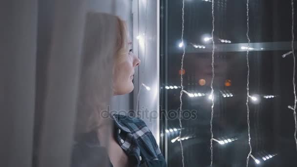 Hermosa mujer atractiva sentada en el alféizar de la ventana decorada con guirnaldas. Año Nuevo, Navidad, Concepto de vacaciones — Vídeo de stock