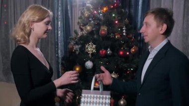 Erkek adam sarışın kız kadın hediye kutusu ile Smartphone Noel ağacı yakınındaki verir. Mutlu bir aile.