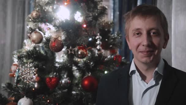 Retrato del hombre sonriente con el pelo rubio en chaqueta cerca de un árbol de Navidad — Vídeo de stock