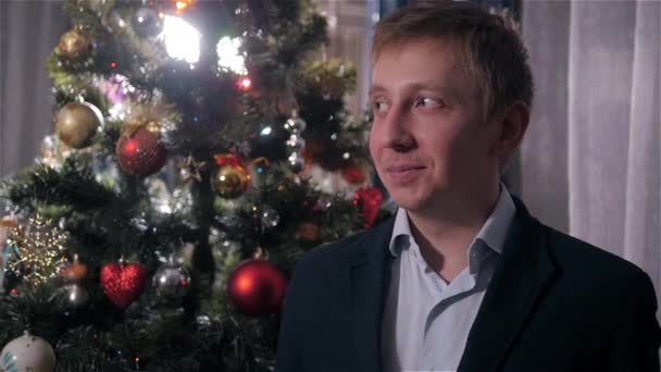 Portrait d'homme souriant aux cheveux blonds en veste près d'un arbre de Noël — Video