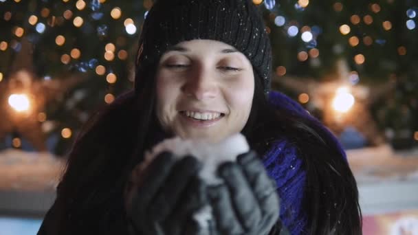 Jonge vrouw sneeuwvlokken waait uit haar handen permanent door kerstboom. Gelukkig Nieuwjaar viering Concept, buiten nacht close-up portret. — Stockvideo