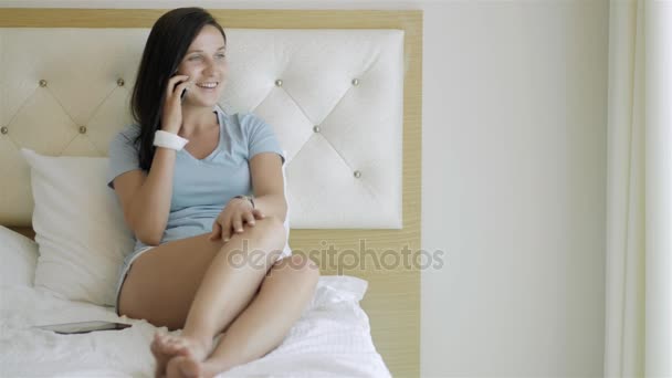 Junges brünettes Mädchen mit Smartphone am Morgen im Bett liegend — Stockvideo