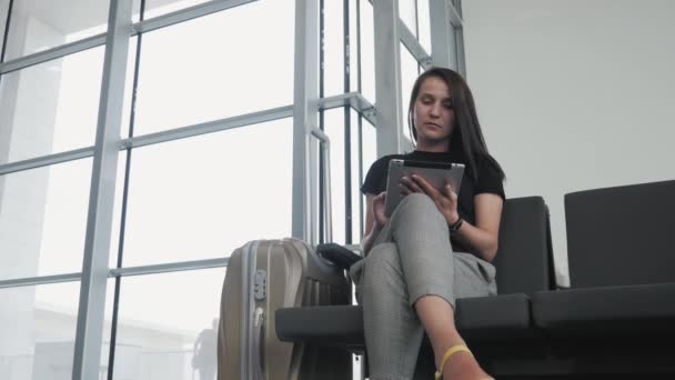 Junge hübsche Geschäftsfrau mit einem Tablet-PC am Flughafen, während sie in der Warteschlange auf die Registrierung wartet, Reisekonzept — Stockvideo
