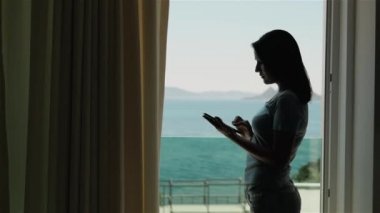 Pencerenin kenarında duran Tablet Pc kullanan genç kadın silüeti