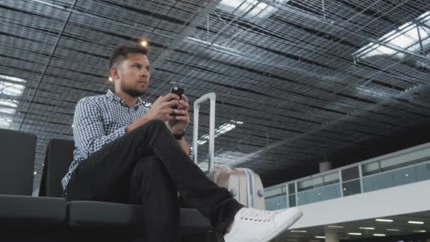 Yakışıklı genç kullanma Smartphone ve çalışma kayıt, seyahat kavramı, teknoloji için onun sıra beklerken havaalanında — Stok video