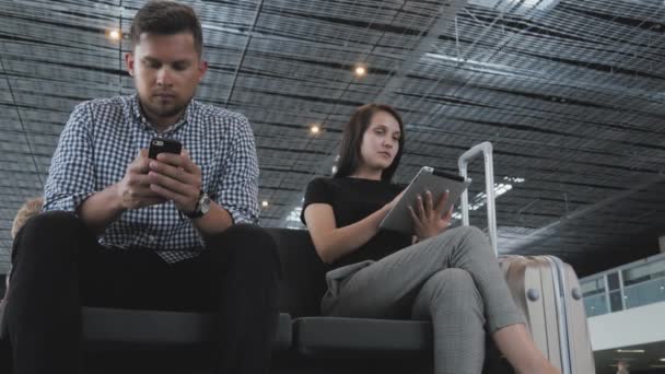Un par de turistas utilizan sus aparatos mientras esperan la cola para el check-in en el aeropuerto, la tecnología, el concepto de viaje — Vídeo de stock