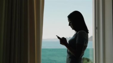 Akıllı telefon kullanan genç kadın silüeti. Beyaz ayakta pencerede Model ve onun Smartphone kullanın