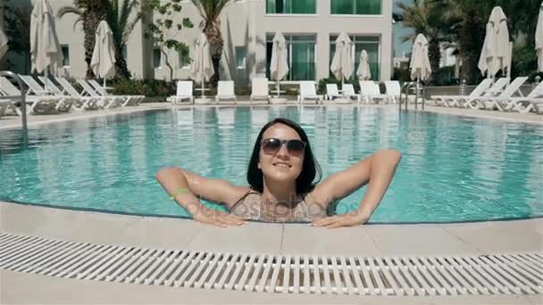 Sexig tjej kommer upp ur poolen. Sommarsemester i semesterorten, tjej simmar i det klara vattnen i poolen, vackra leenden — Stockvideo